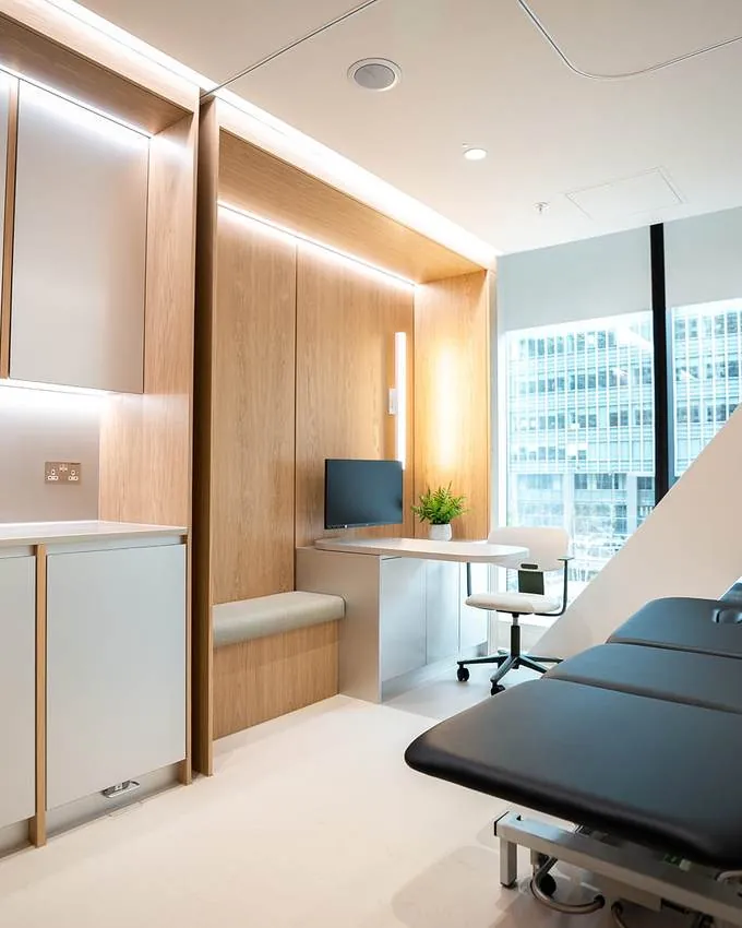 A clinical consulting room with a treatment couch and a window over Canary Wharf.